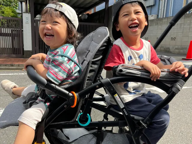 2人乗りベビーカーに乗る笑顔の子どもたちの写真